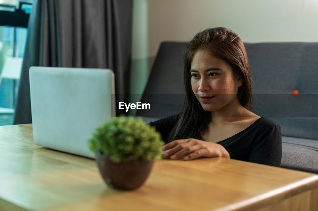 Smiling young woman using laptop while sitting at home