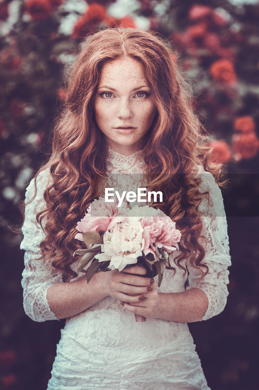 Portrait of bride holding bouquet standing outdoors