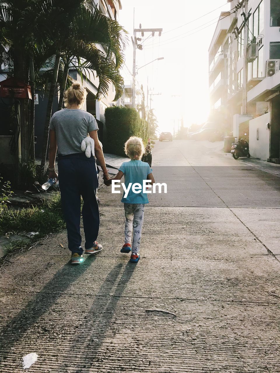 Rear view of mother and daughter walking on footpath in city