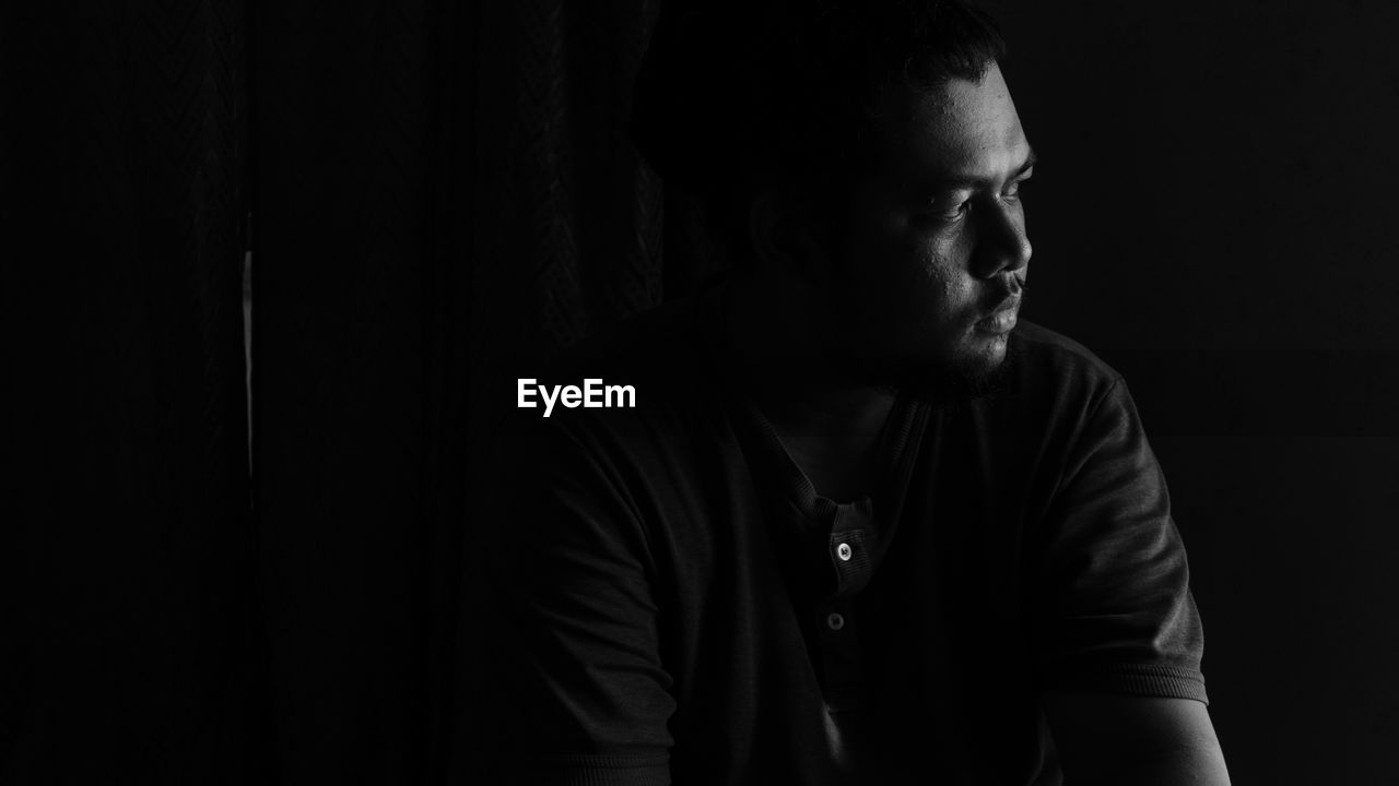 Young man looking away against black background