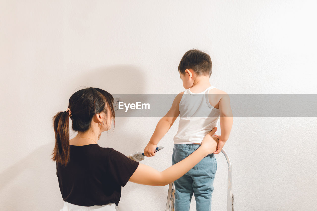 Young mother teaching son to paint the wall. mom and child moment.