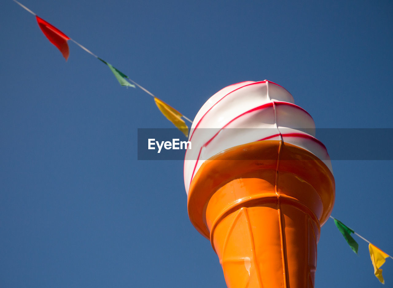 Ice cream cone statue, with multi coloured flag bunting and a clear blue sky behind