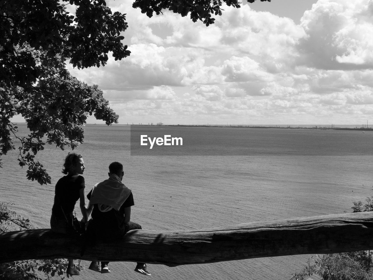 REAR VIEW OF MEN SITTING ON SEA SHORE AGAINST SKY