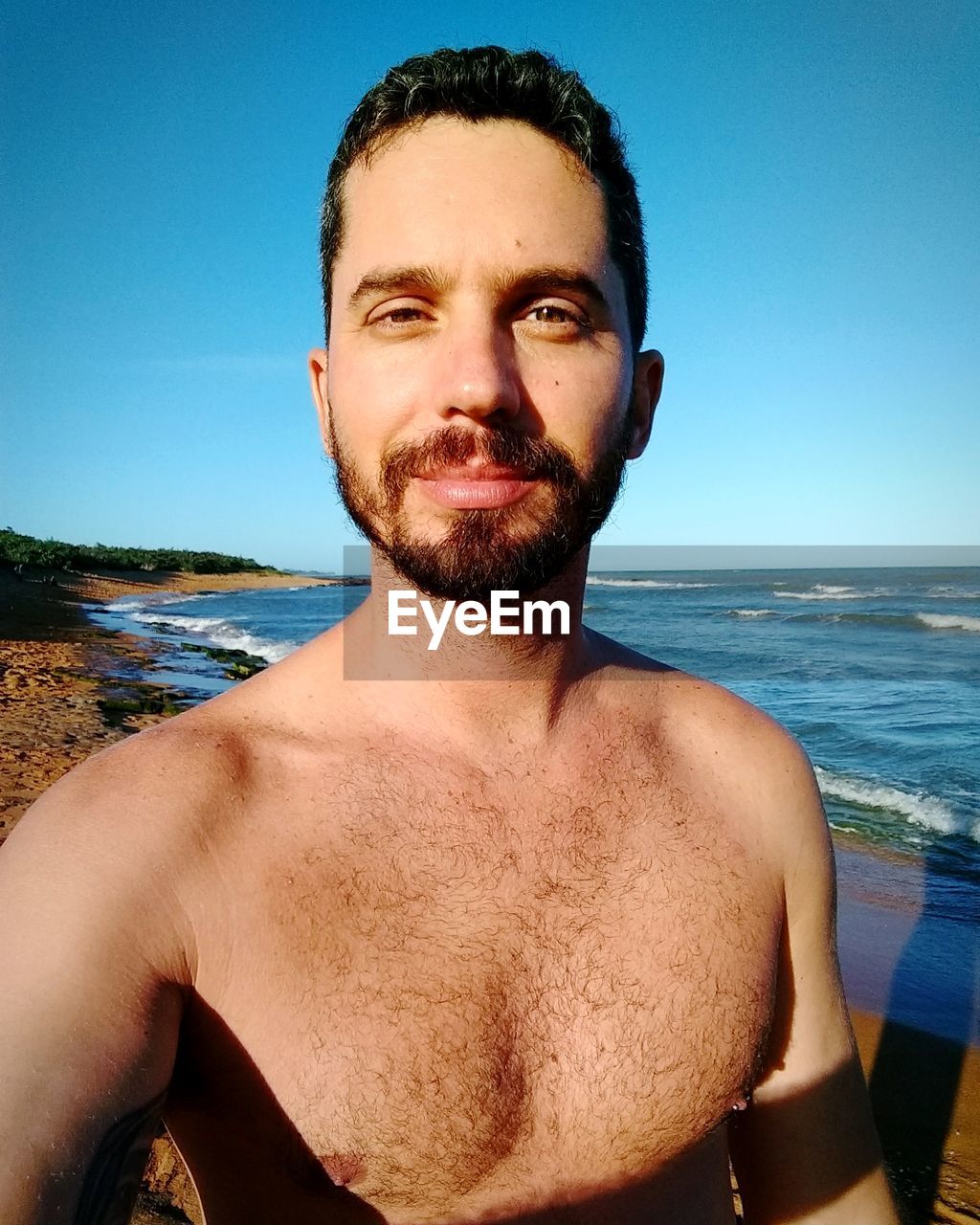 Portrait of smiling man on beach against clear blue sky