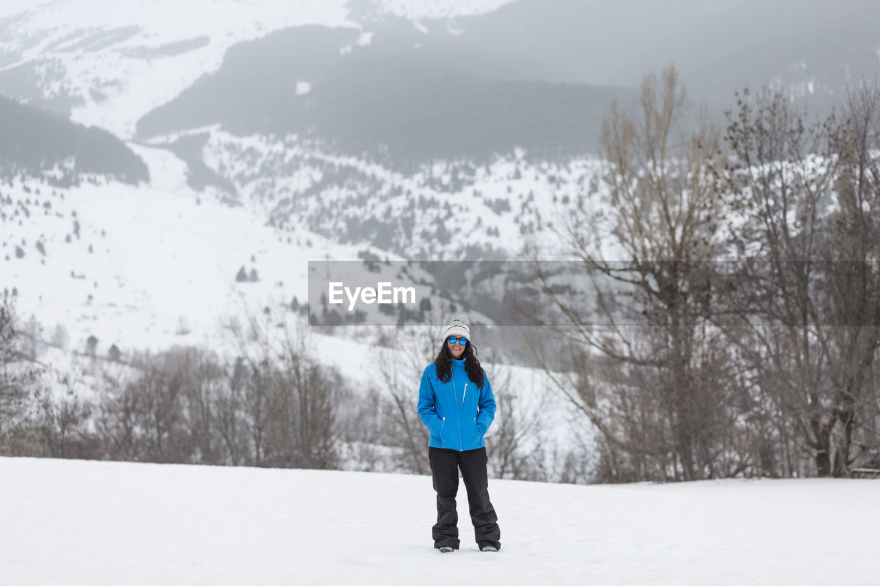 Portrait of smiling woman standing on snowcapped mountain during winter