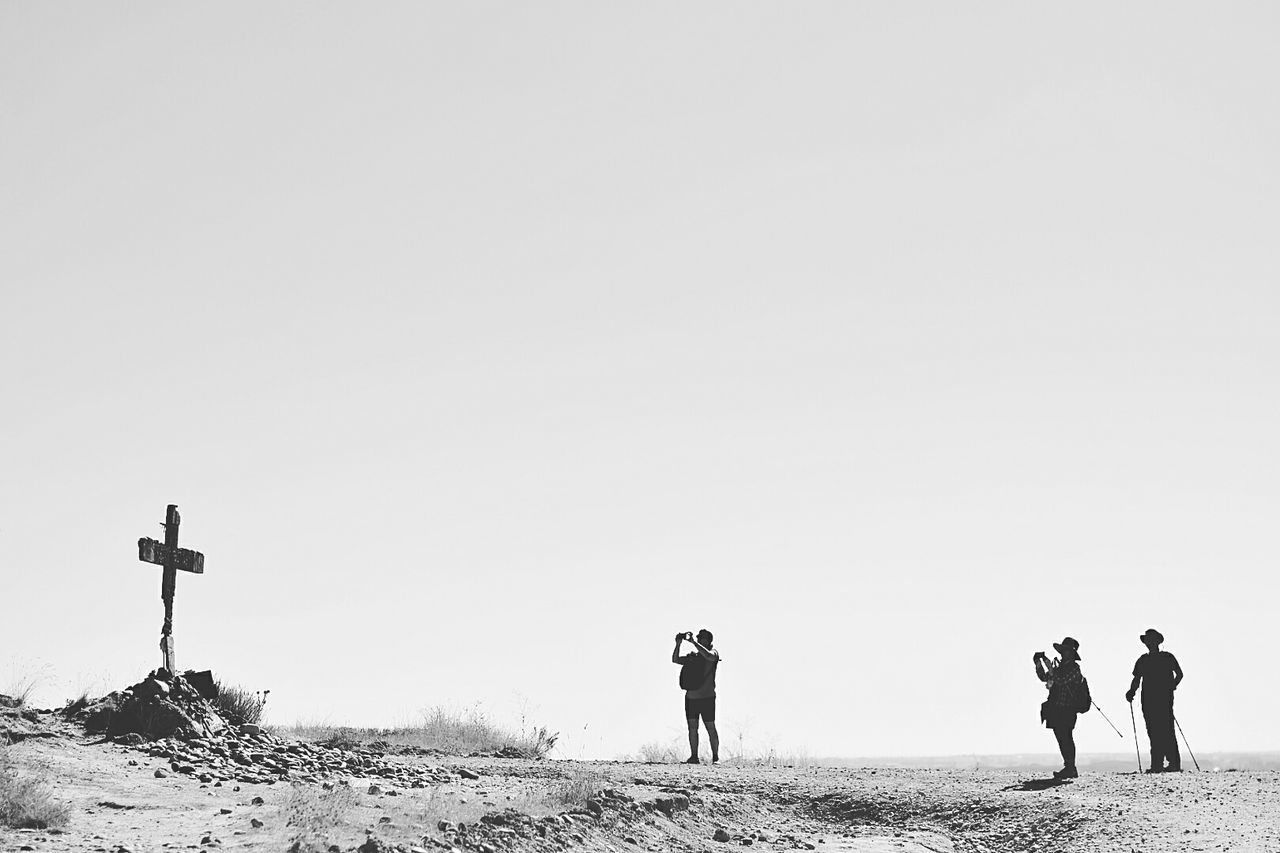Side view of men photographing cross in arid landscape