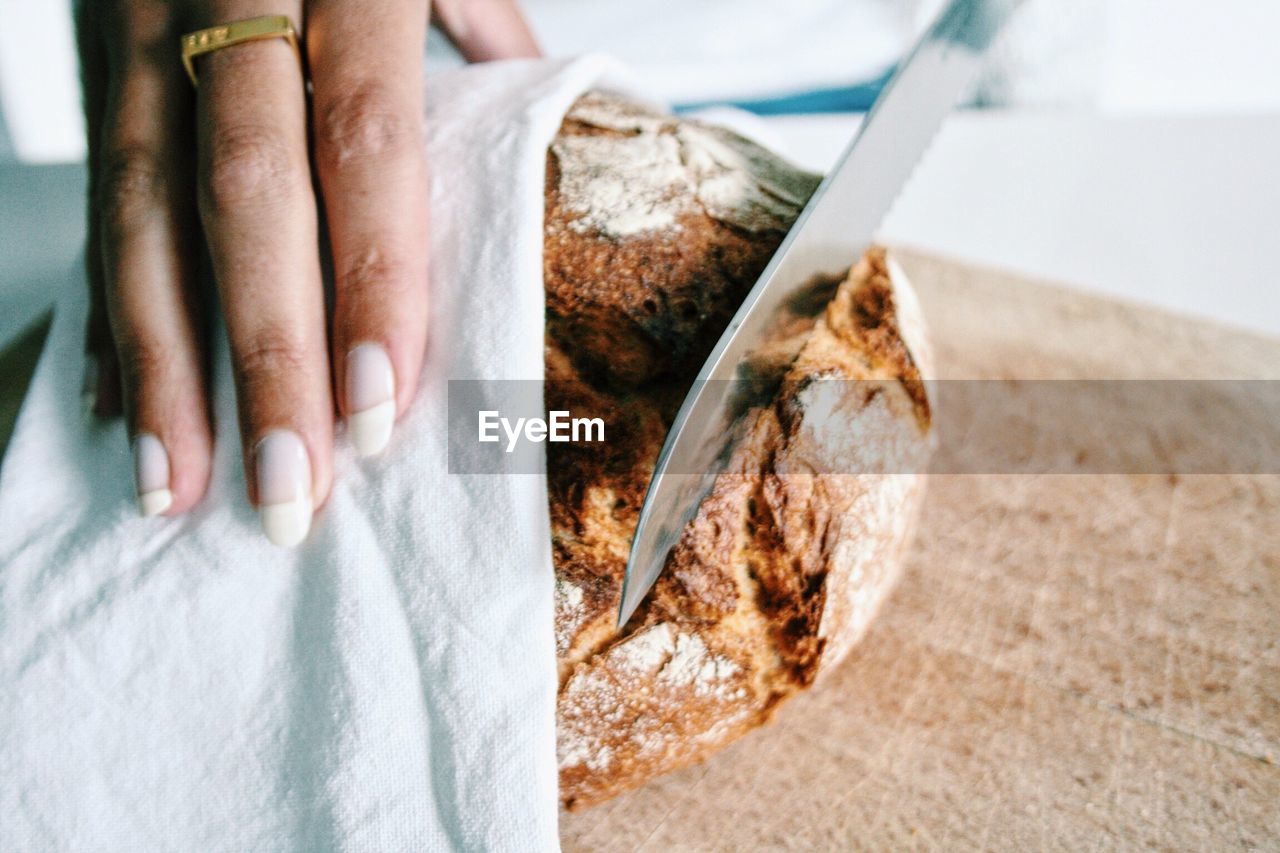 Cropped hand on woman cutting bread on cutting board