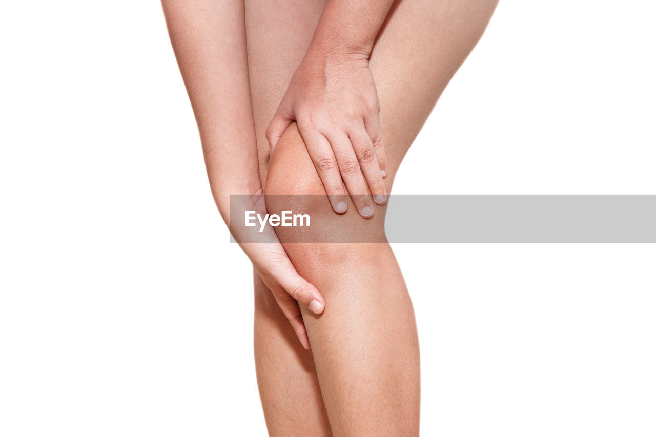 Midsection of woman holding knee while standing against white background