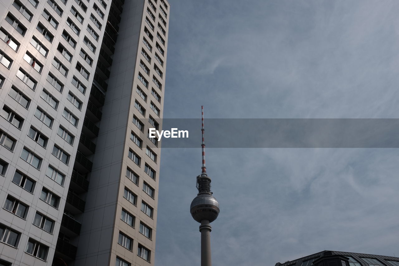 Low angle view of fernsehturm tower by building against sky