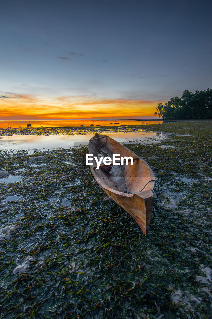 Nautical vessel on beach against sky during sunset