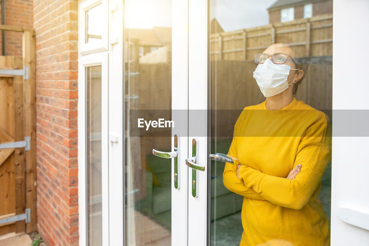 Woman wearing mask standing by window at home