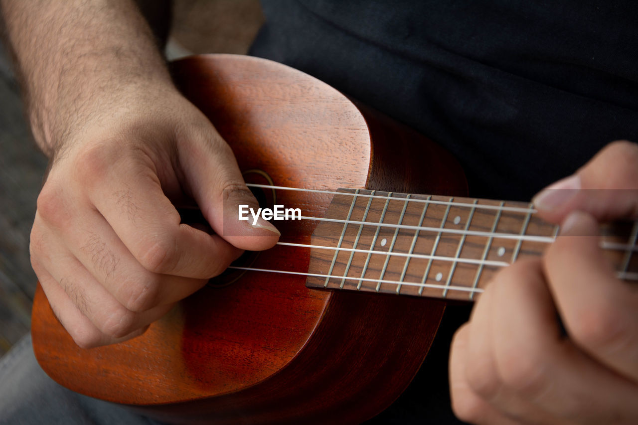 Cropped hand of man playing ukulele outdoors