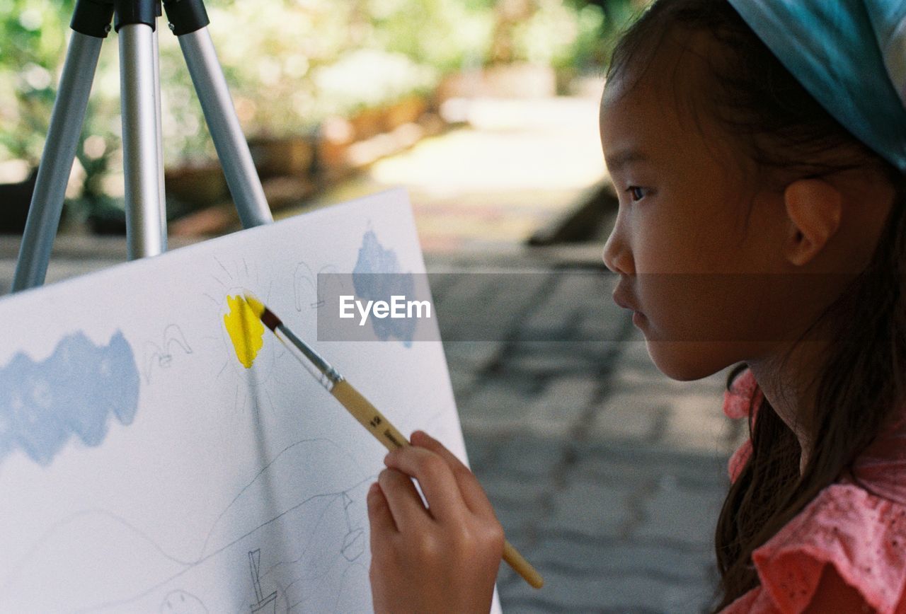 Close-up of girl painting on canvas outdoors