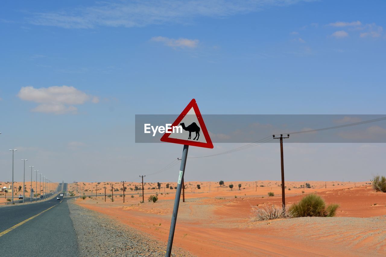 Road sign by street against sky in desert