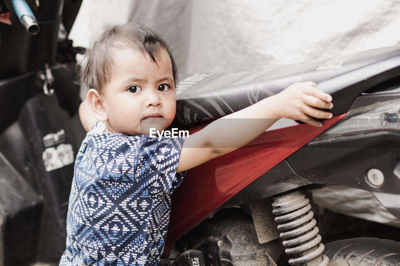 Portrait of cute boy standing by covered motorcycle