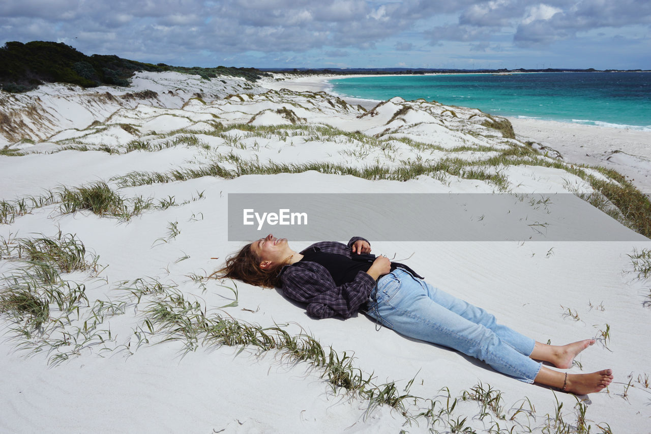 Woman lying on sand at beach against sky