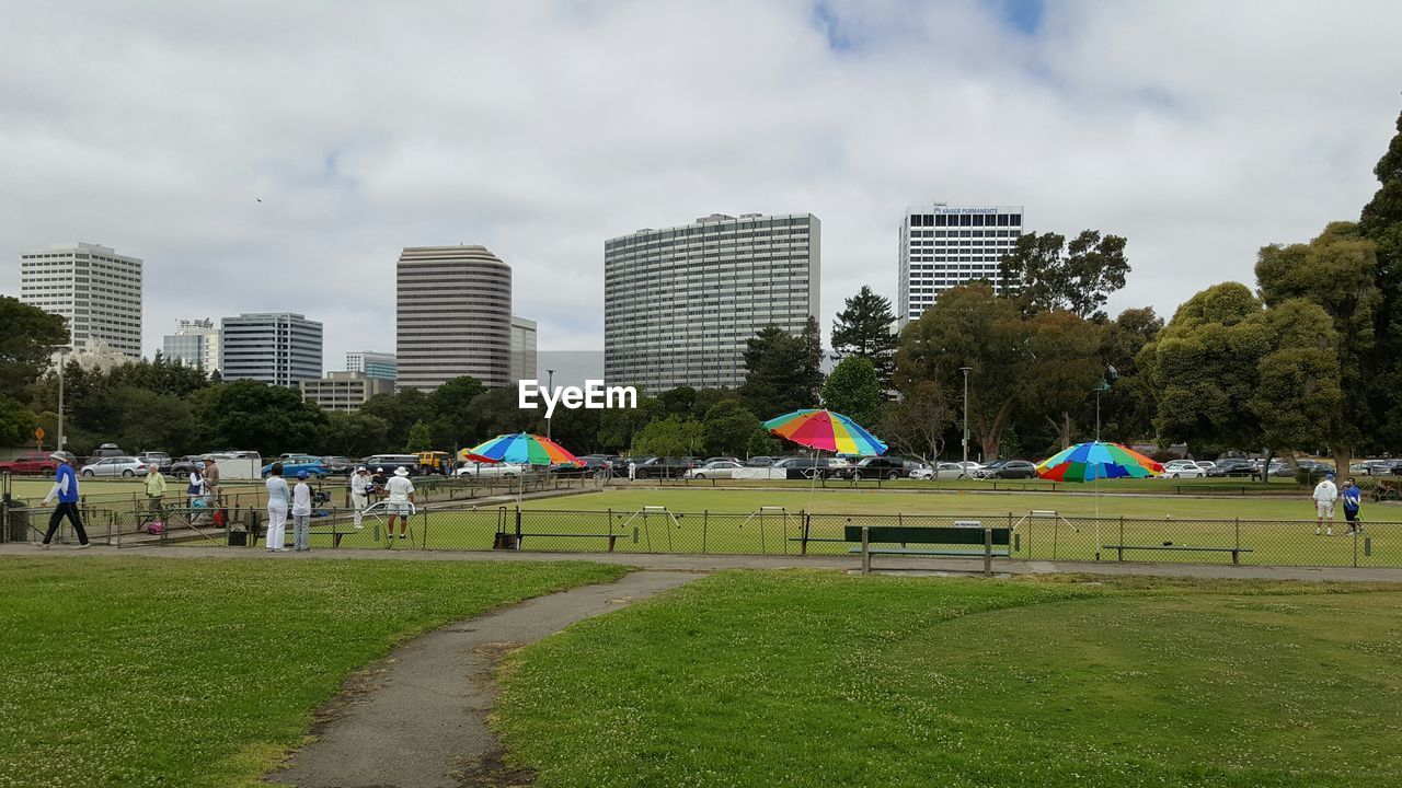 Green field and buildings against cloudy sky