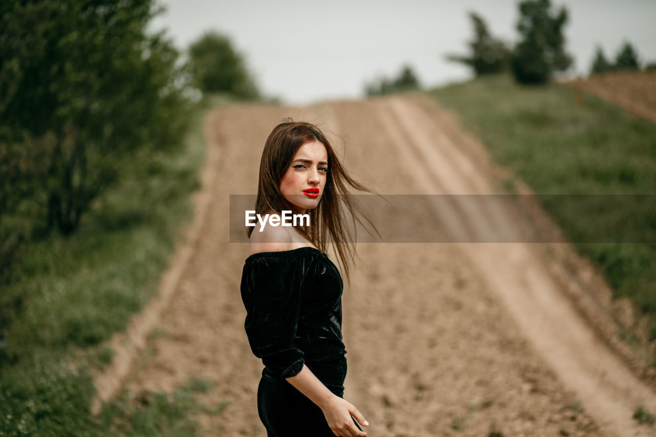 Portrait of young woman standing on dirt road