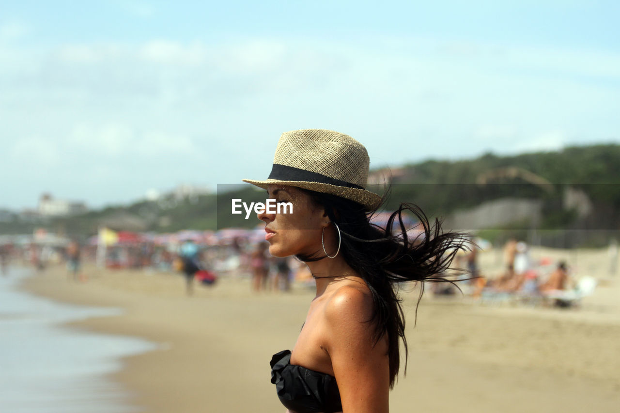 Side view of woman with eyes closed wearing hat standing at beach