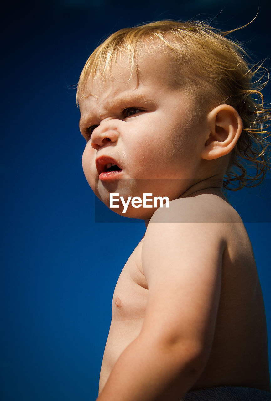 Side view of shirtless baby boy against blue sky