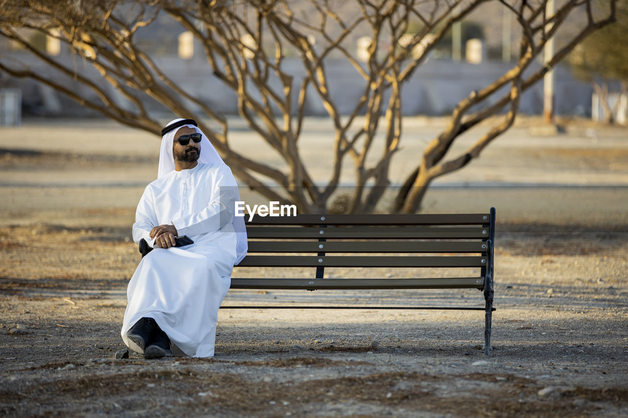 REAR VIEW OF WOMAN SITTING ON BENCH