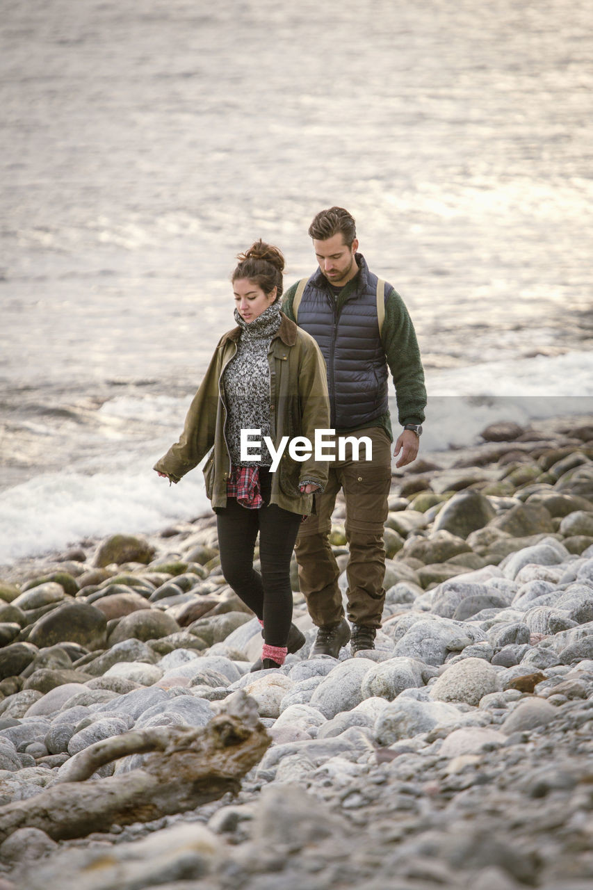 Couple walking on rocky shore during sunset