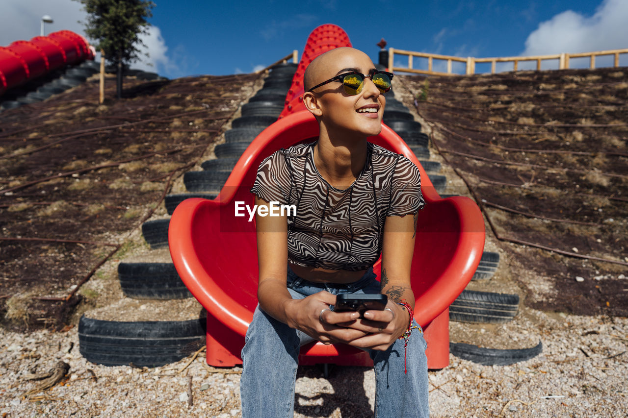 Smiling young woman wearing sunglasses holding smart phone at park