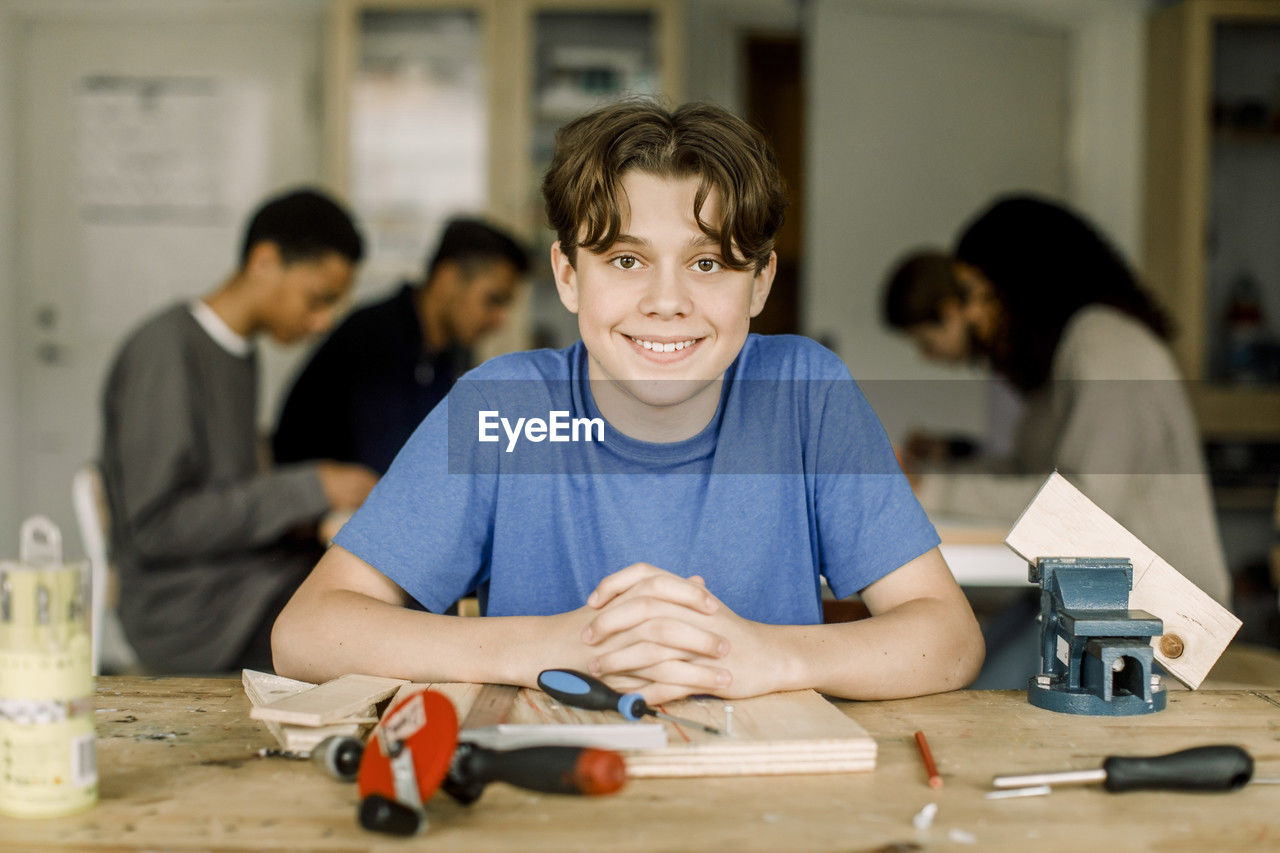 Portrait of smiling male teenage student with tools on table during carpentry class at high school