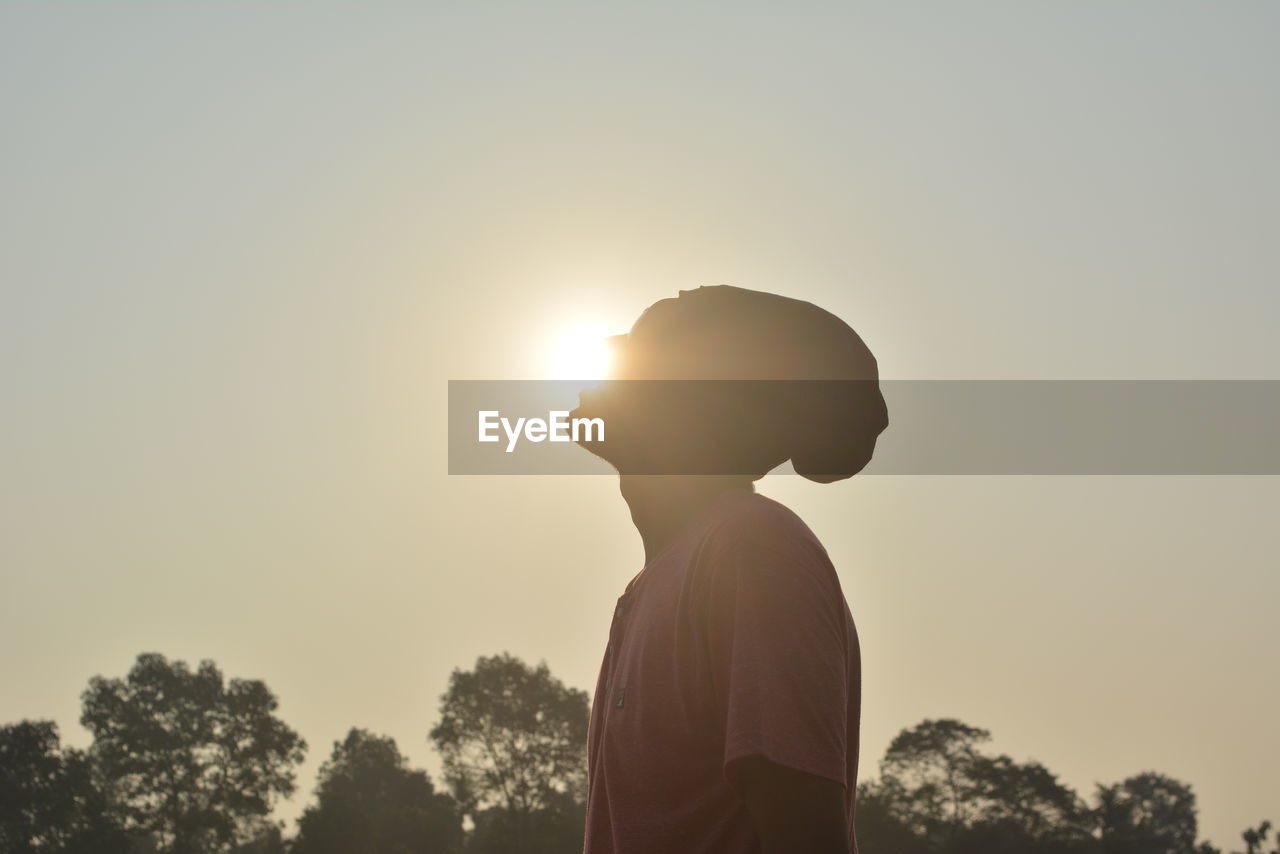 SILHOUETTE BOY STANDING BY TREE AGAINST CLEAR SKY