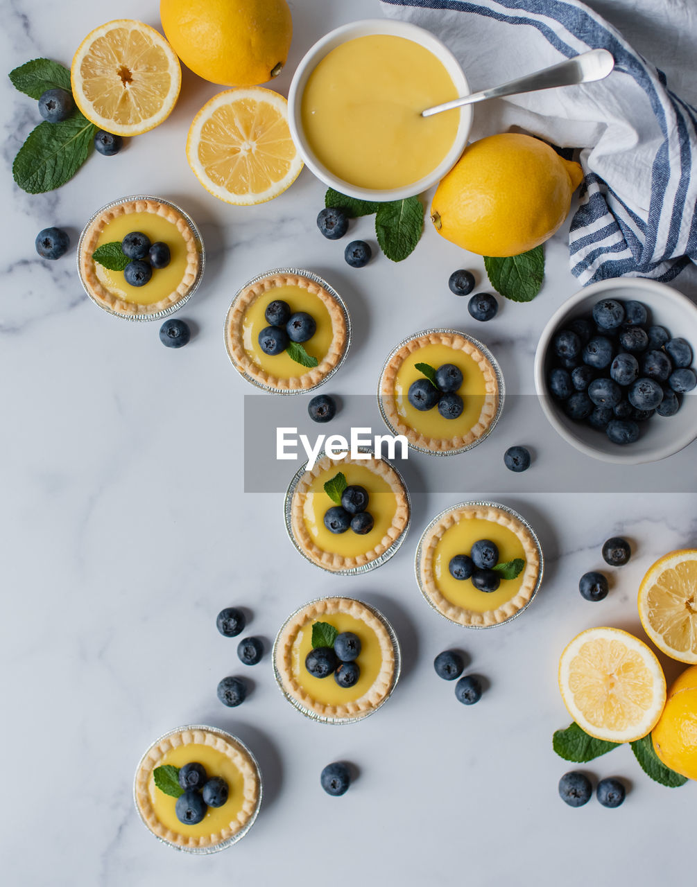 Overhead view of mini lemon tarts with blueberries on marble counter.