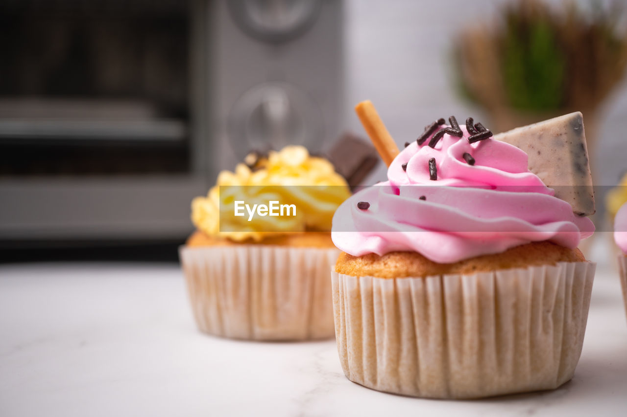 Delicious homemade cupcakes with colorful cream and topping with candy and chocolate cookies.