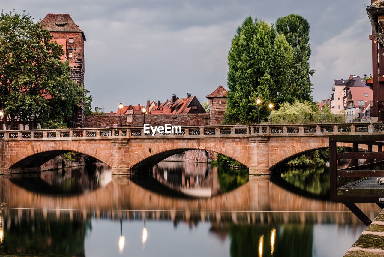 Arch bridge over river amidst buildings in city against sky