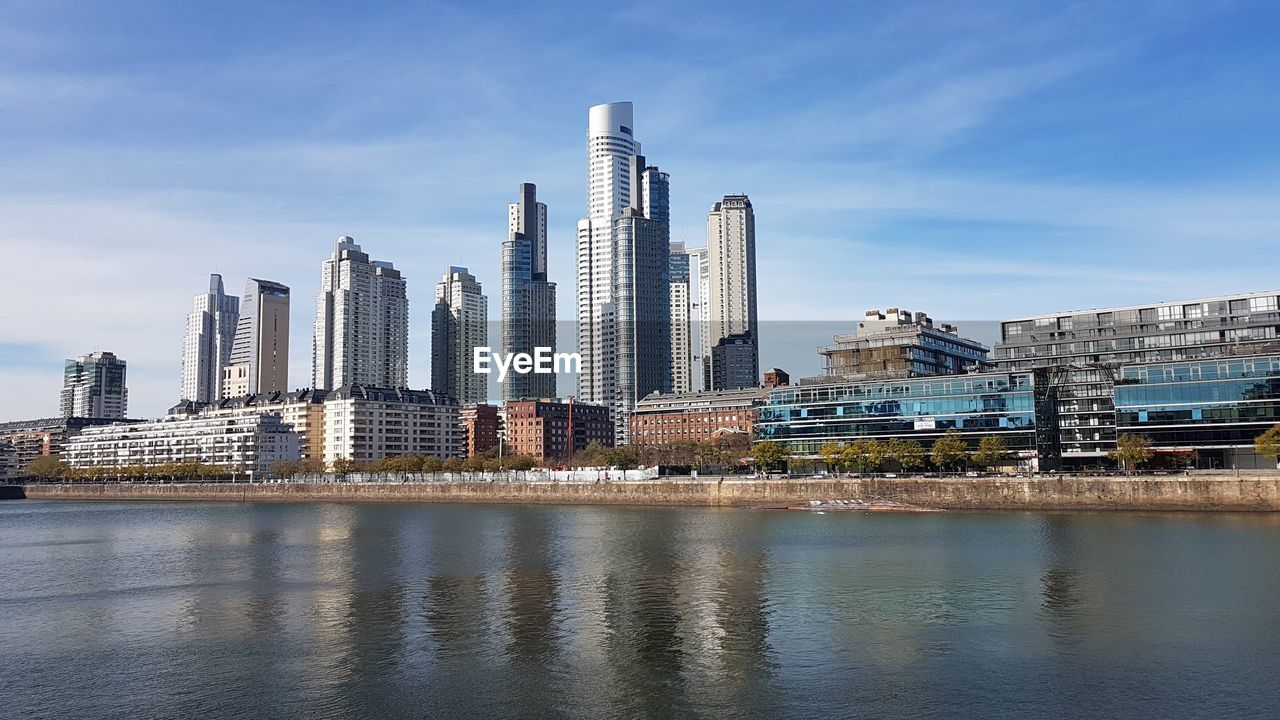 Modern buildings by river against sky in city