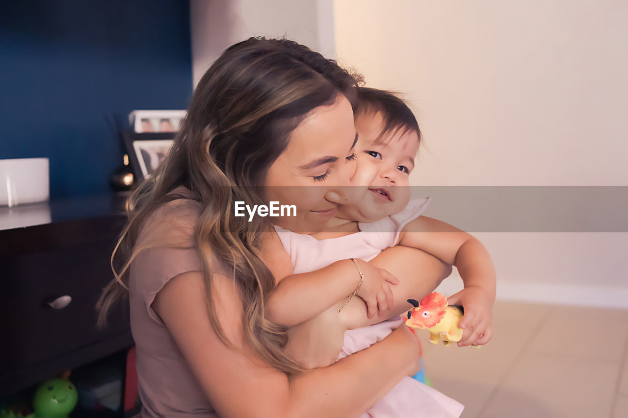 Mom hugging baby daughter who is holding a dinosaur