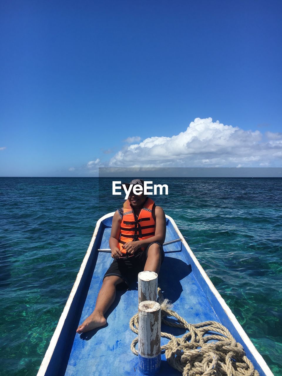 Man sitting on boat in sea against blue sky