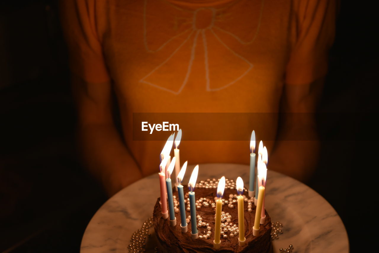Midsection of woman holding illuminated birthday cake