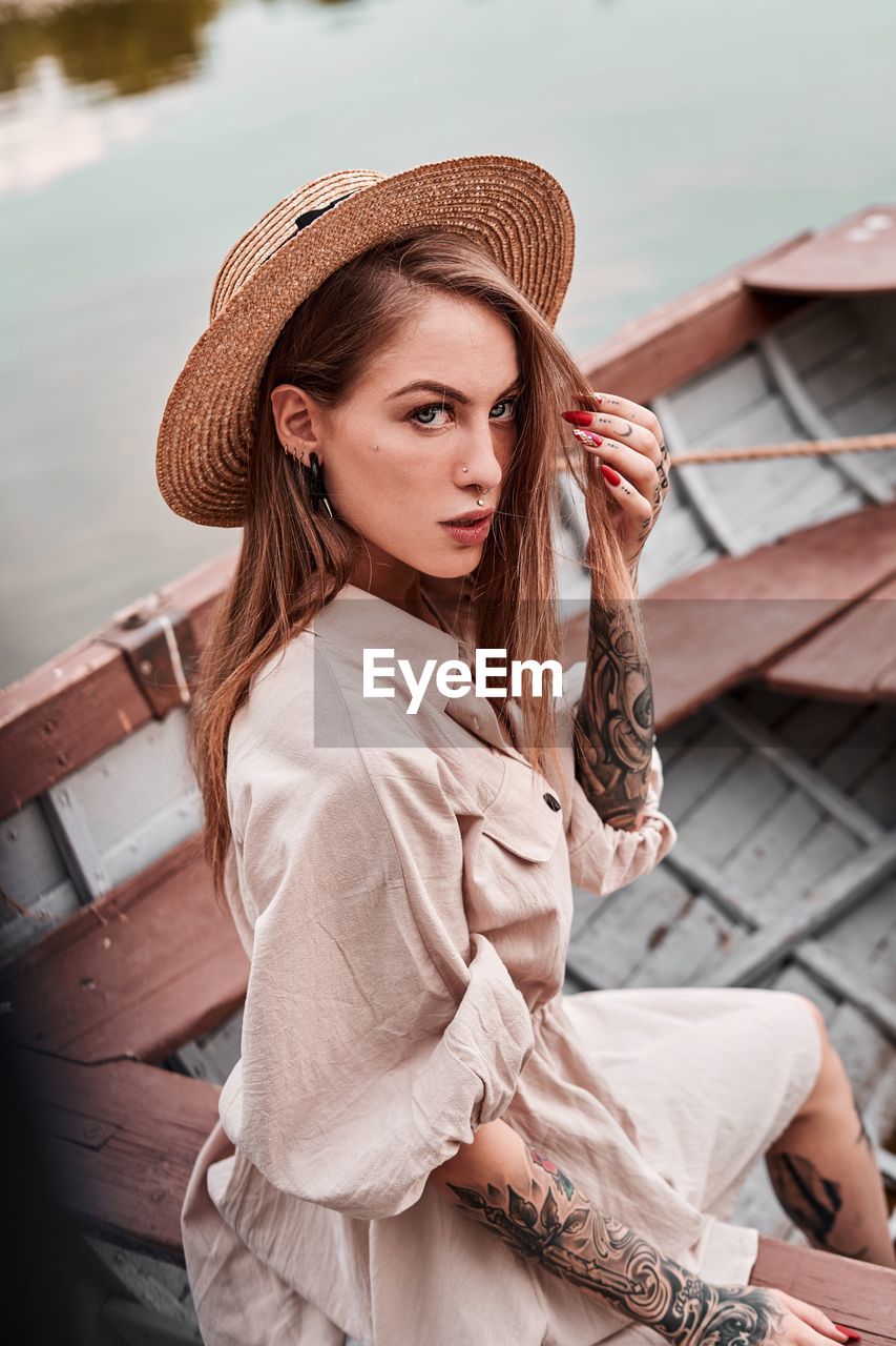 Portrait of young woman wearing hat while sitting in boat