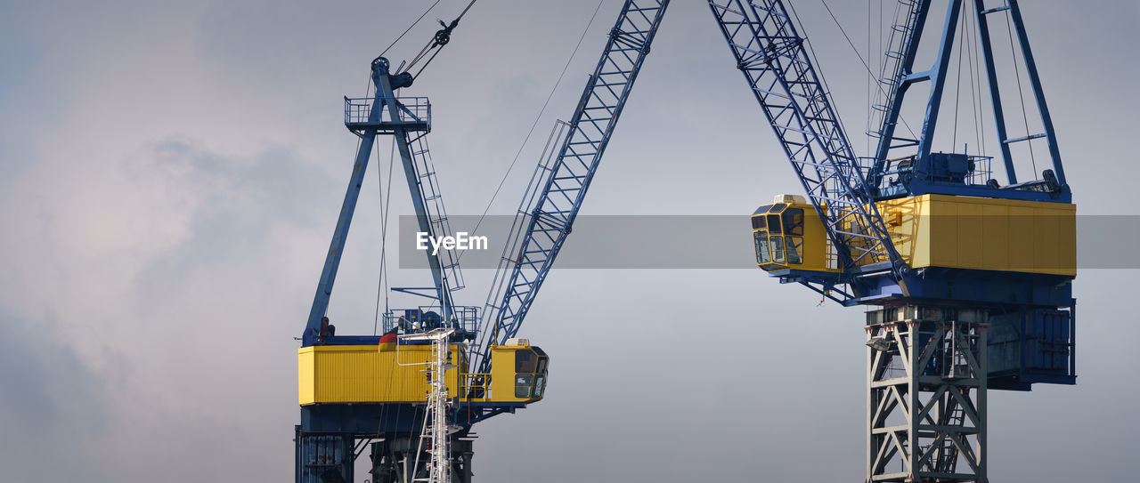 LOW ANGLE VIEW OF CRANES AGAINST SKY