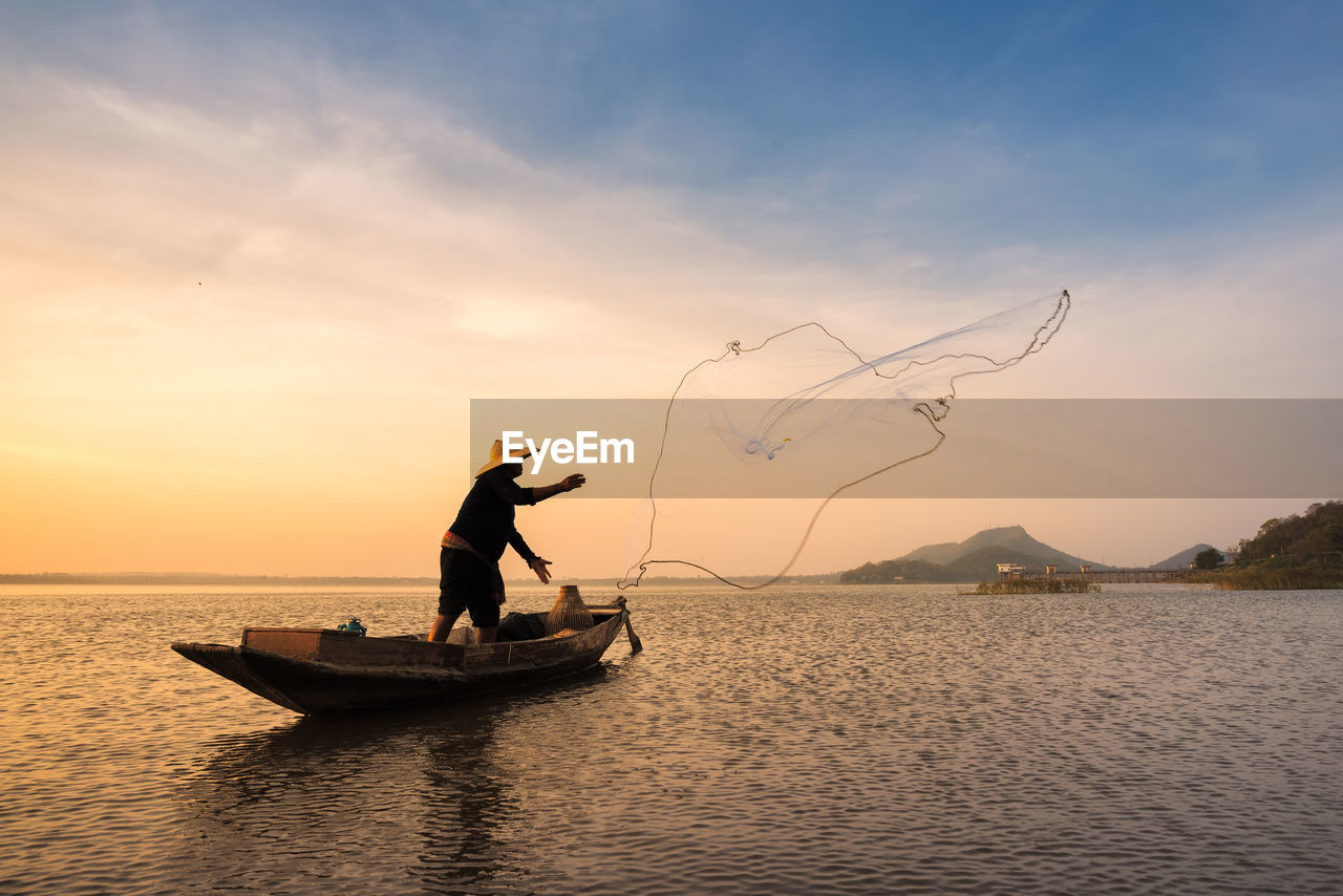 Fisherman fishing against cloudy sky during sunset