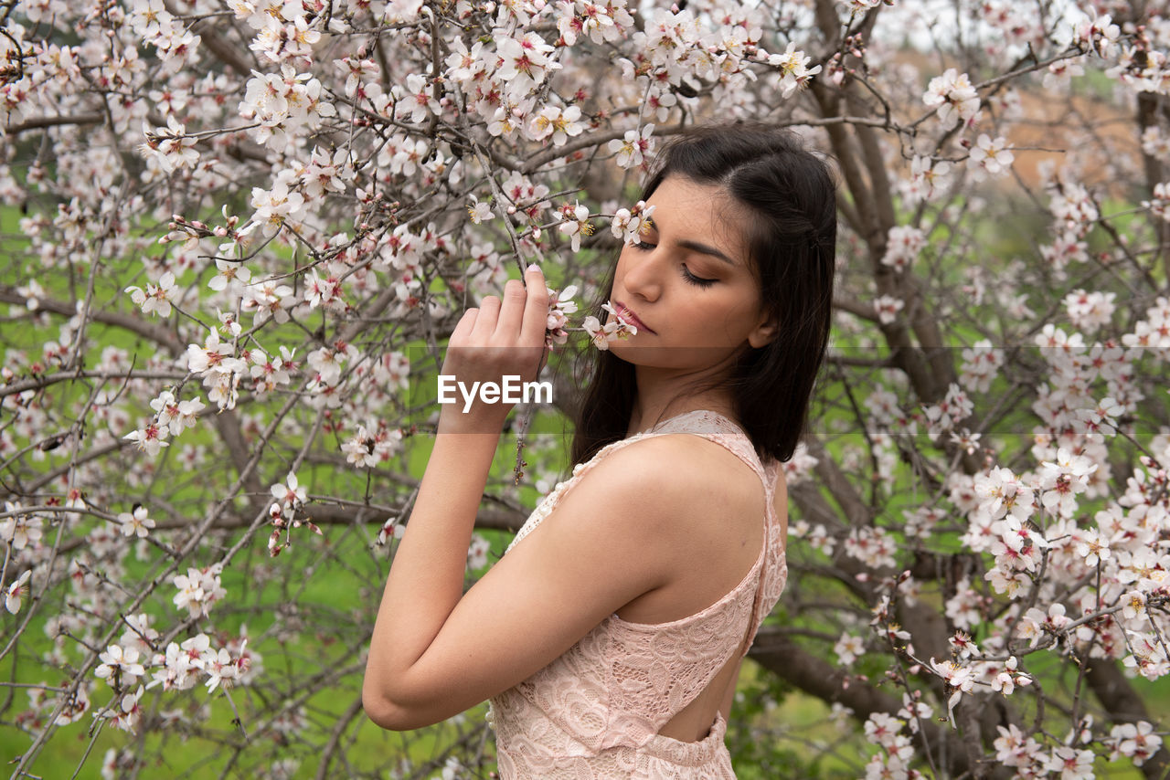 Low angle view of woman standing by pink flowering tree