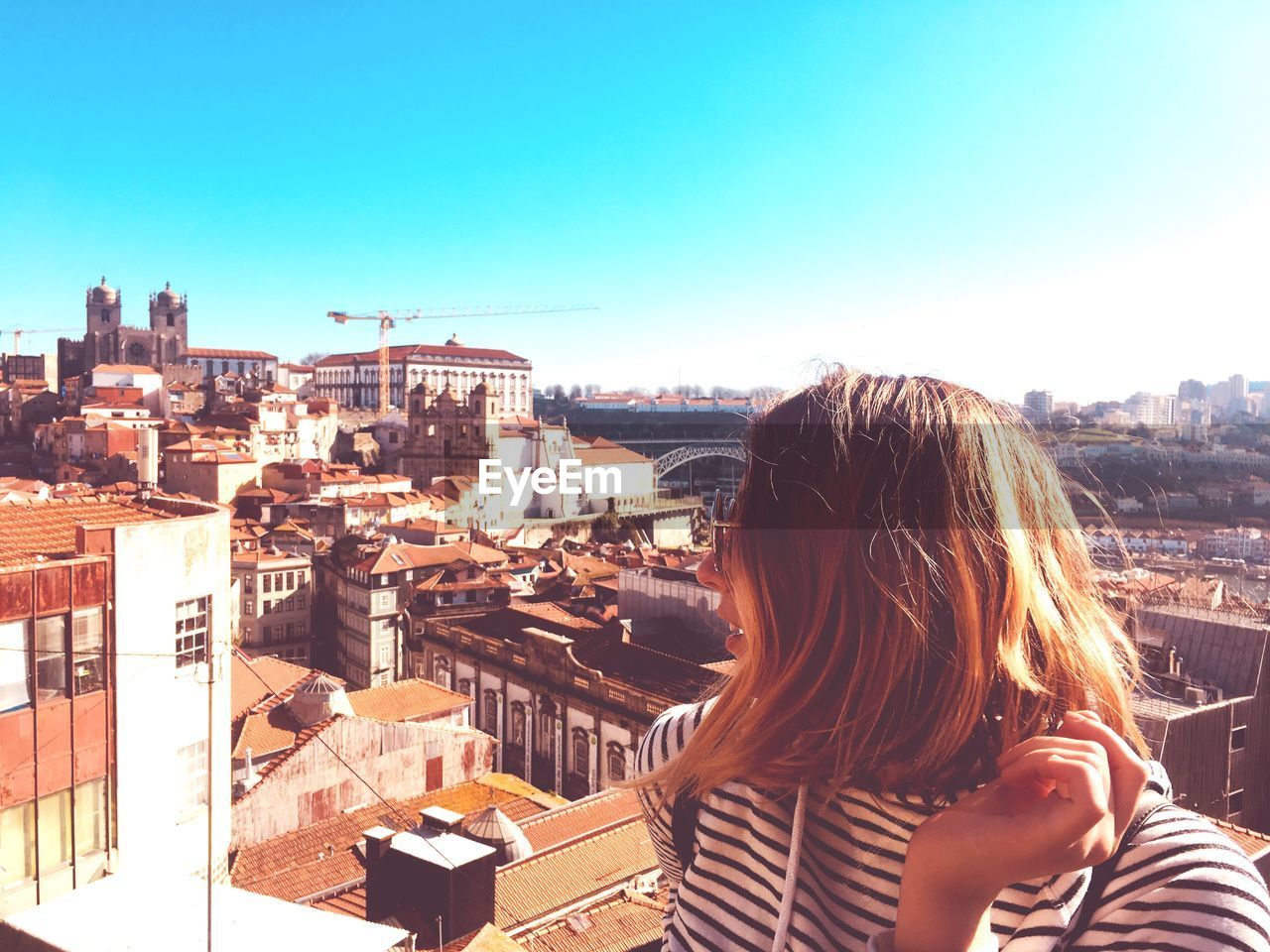 Young woman wearing sunglasses while standing against cityscape during sunny day