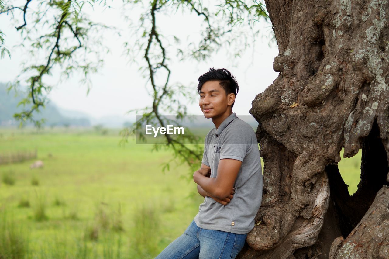 FULL LENGTH OF YOUNG MAN STANDING ON TREE TRUNK