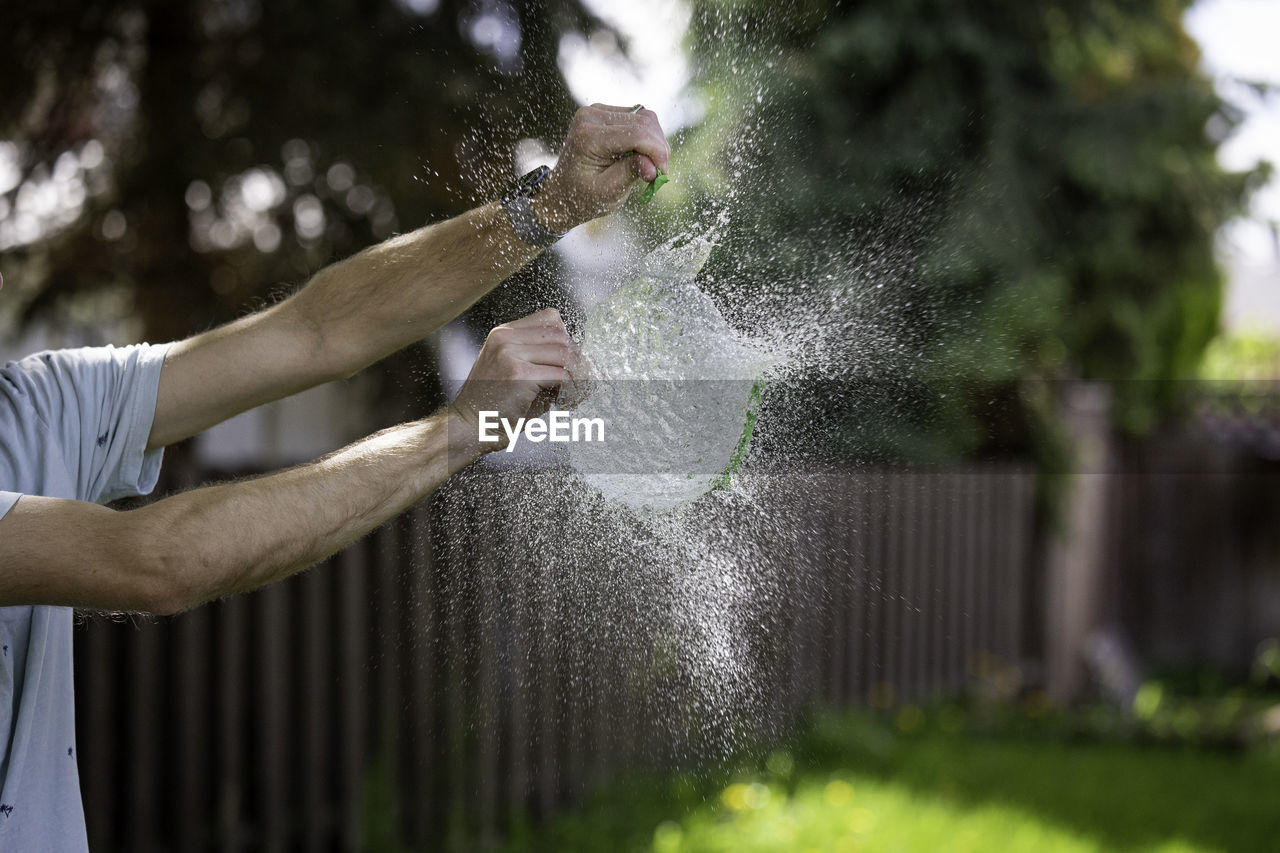 Midsection of man bursting water bomb in yard