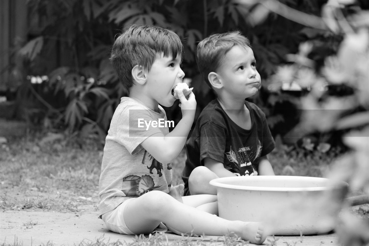 Brothers eating food while sitting on land