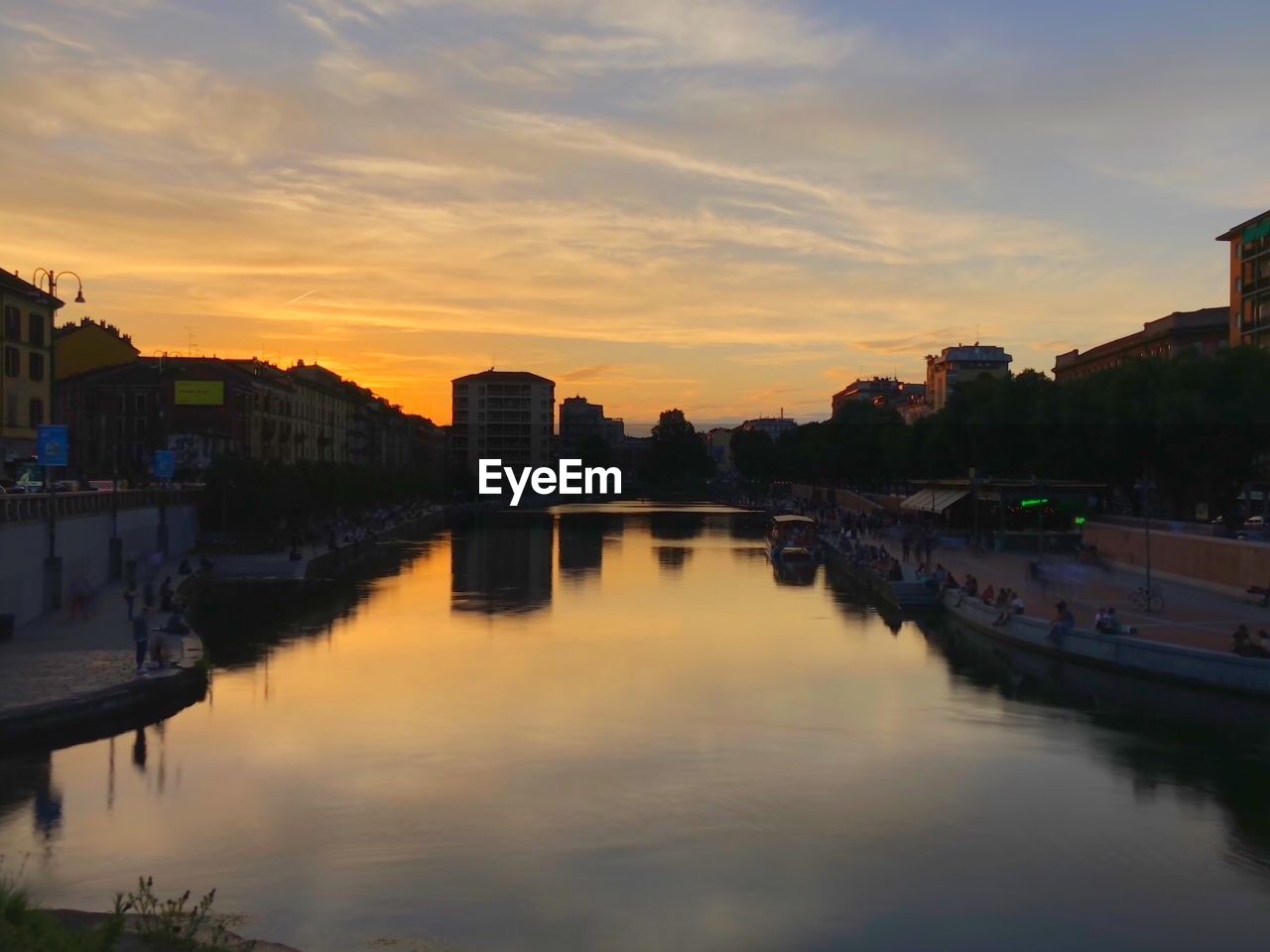 Scenic view of river by buildings against sky during sunset