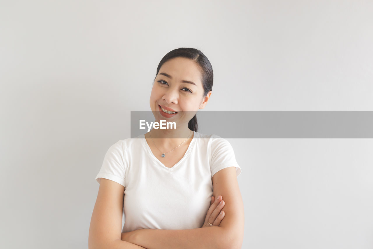 PORTRAIT OF SMILING WOMAN AGAINST WHITE BACKGROUND