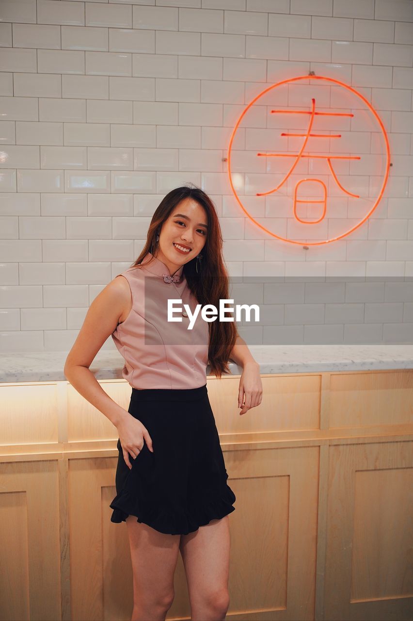 Portrait of smiling young woman standing against wall