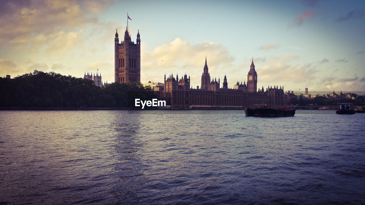 Ferries sailing on thames river by houses of parliament and big ben against sky