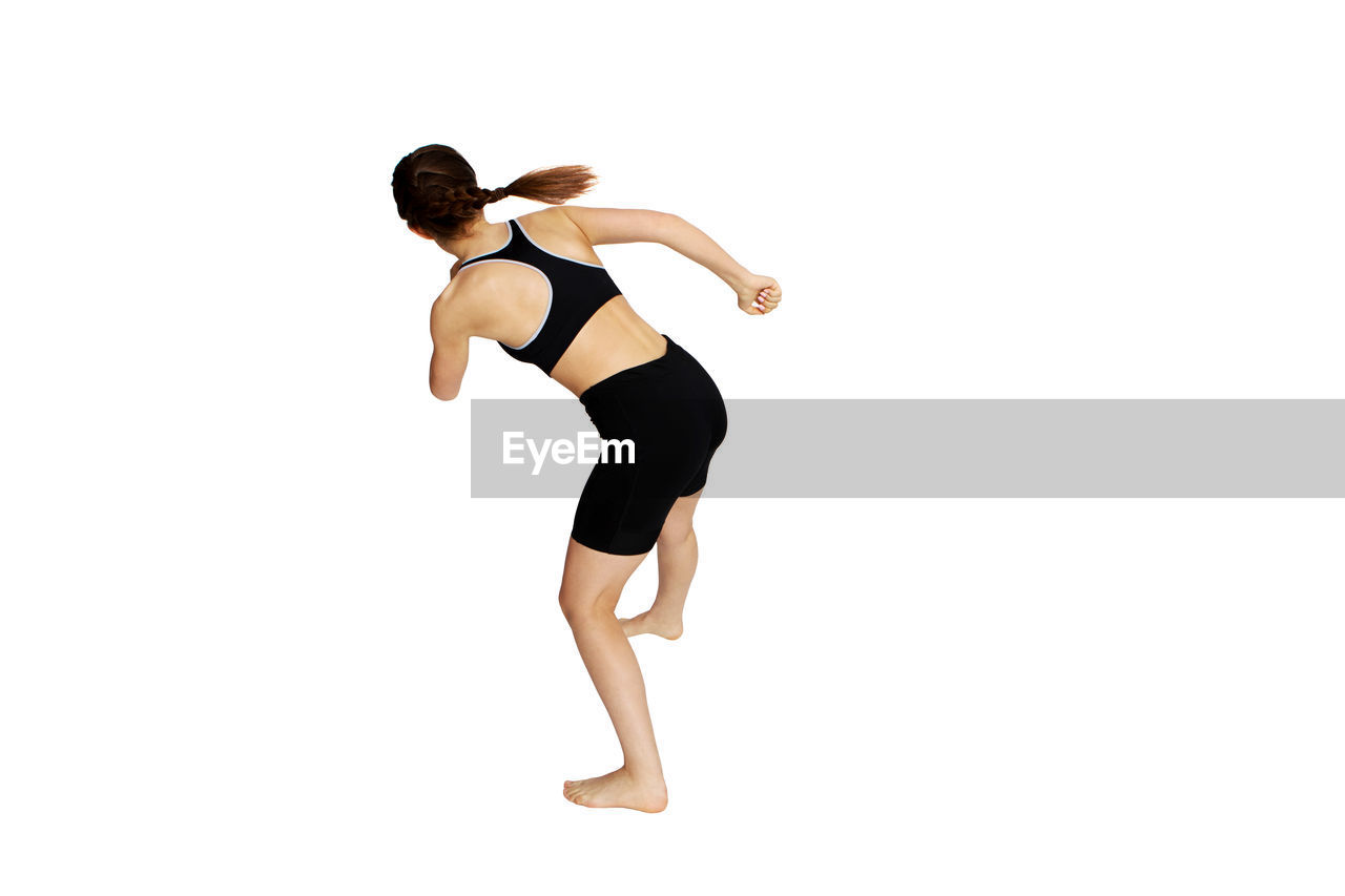 Teenage girl wearing sports clothing exercising against white background