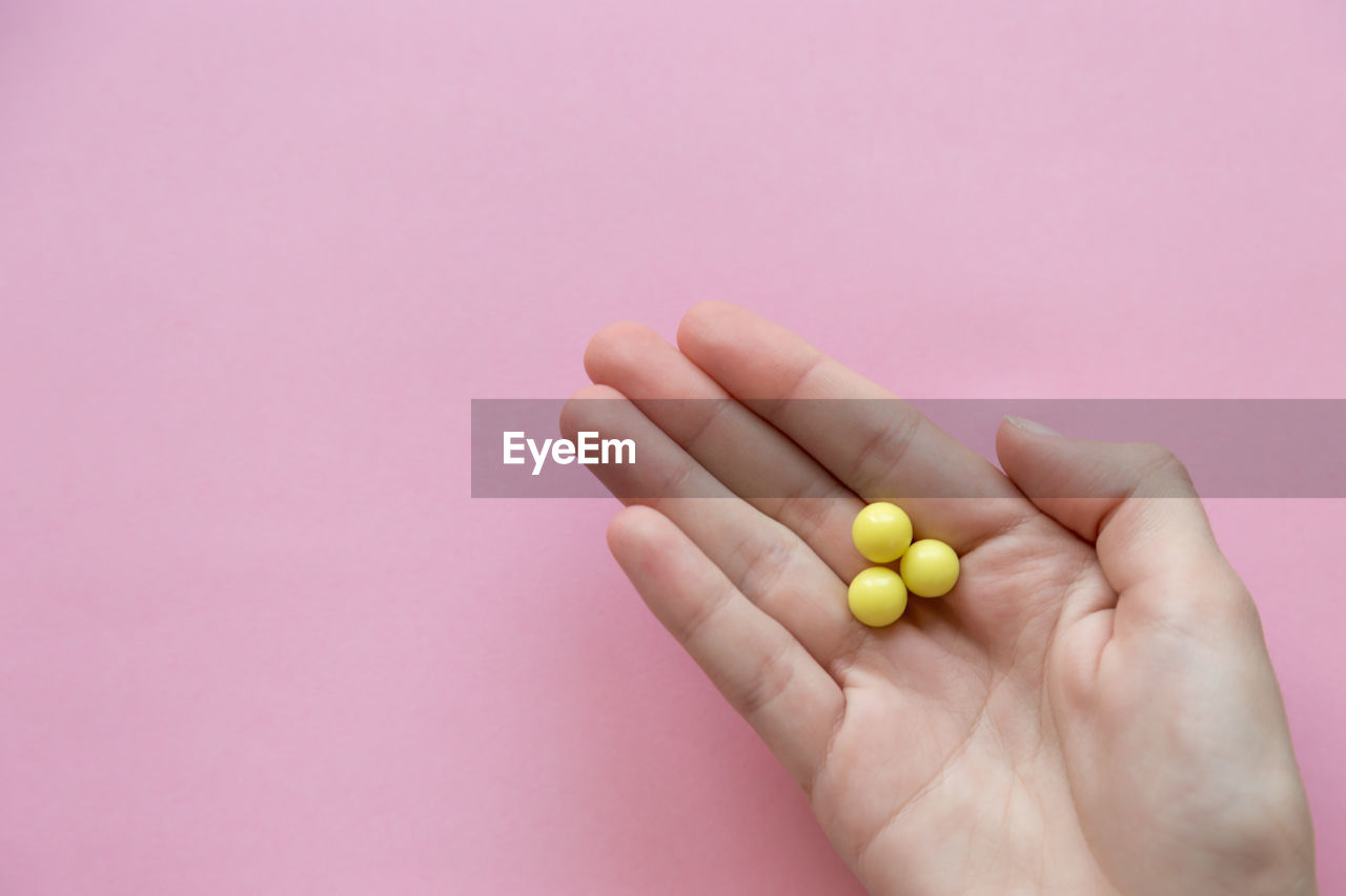 Cropped hand of woman holding candies against pink background